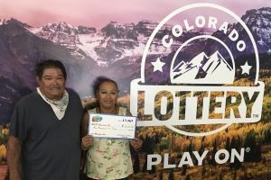 Patricia M. de La Junta sosteniendo un cheque de gran tamaño por $10,000 frente al fondo de la Lotería de Colorado.