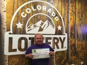 Mark K. sosteniendo un cheque gigante de $12,000 frente al fondo de Colorado Lottery