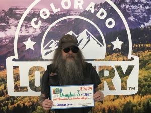Douglas S. holding an oversized check for $1,265 in front of Colorado Lottery background