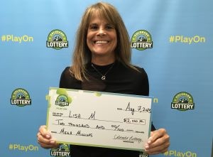 Lisa M. de Englewood sosteniendo un cheque de gran tamaño por $2,000 frente al fondo de la Lotería de Colorado.