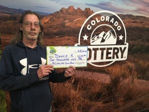 Dennis H. sosteniendo el cheque gigante de $1,000 frente al fondo de Colorado Lottery