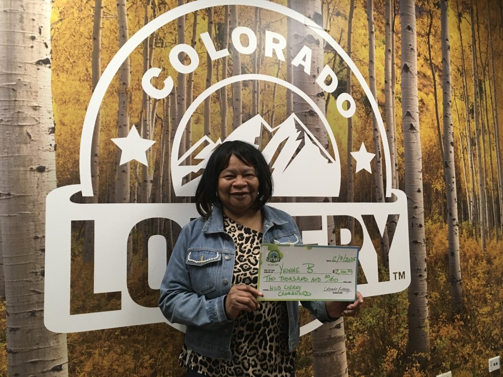 El ganador sostiene un cheque de gran tamaño frente a un fondo de la Lotería de Colorado