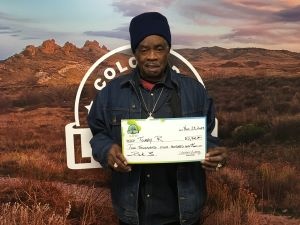 Tommy R. sosteniendo el cheque de $2,900 frente al fondo de Colorado Lottery