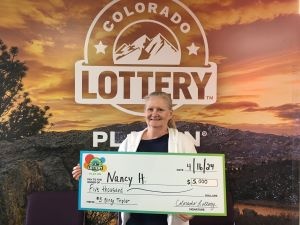 Nancy H. sosteniendo el cheque gigante de $5,000 frente al fondo de Colorado Lottery