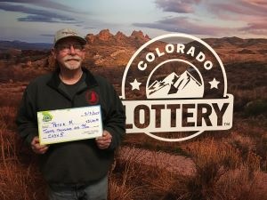 Peter M. sosteniendo un cheque de gran tamaño por $20,000 frente al fondo de la Lotería de Colorado