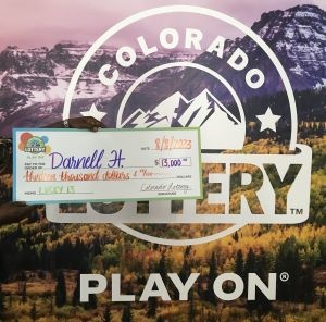 Darnell H. de Pueblo sosteniendo un cheque de gran tamaño por $13,000 frente al fondo de la Lotería de Colorado (sin mostrar su rostro ni su cuerpo).