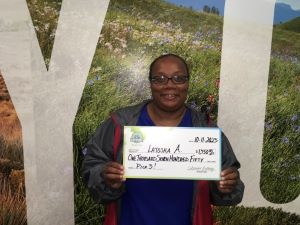 Latosha A. sosteniendo un cheque de gran tamaño por $1,750 frente al fondo de la Lotería de Colorado