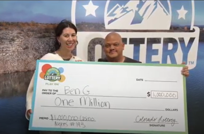 Ben S. de Denver sosteniendo un cheque de gran tamaño por $1,000,000 frente al fondo de la Lotería de Colorado.
