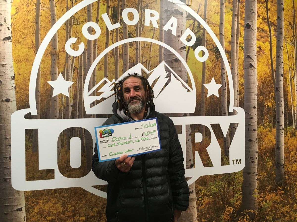 Octavio A. sosteniendo el cheque gigante de $1,000 frente al fondo de Colorado Lottery