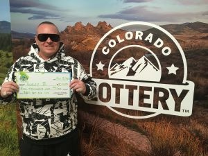 Ashley E. holding check for $5,000 in front of Colorado Lottery background