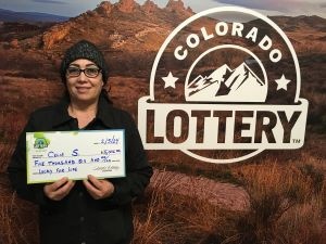 Celia S. sosteniendo un cheque de gran tamaño por $5,000 frente al fondo de la Lotería de Colorado