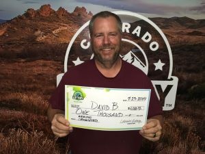 David B. holding an oversized check for $1,000 in front of Colorado Lottery background