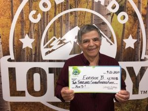 Enrique B. of Boulder holding an oversized check for $2,750 in front of Colorado Lottery background