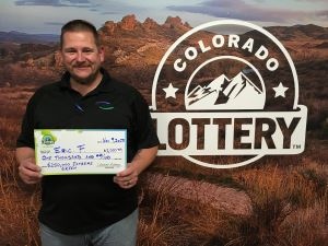 Eric F. sosteniendo el cheque de $1,000 frente al fondo de Colorado Lottery