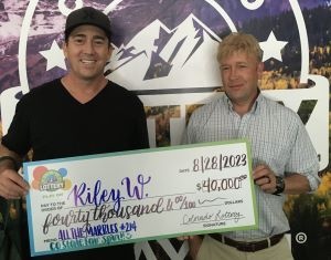 Riley W. of Pueblo holding an oversized check for $40,000 in front of Colorado Lottery background.