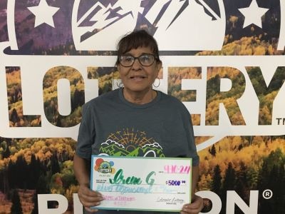 Irene G. holding an oversized check for $5,000 in front of Colorado Lottery background