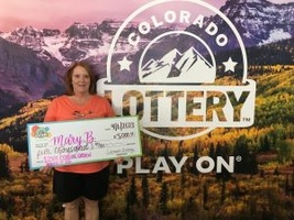 Mary B. of Colorado Springs holding an oversized check for $5,000 in front of Colorado Lottery background.