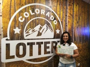 Michelle G. sosteniendo un cheque de gran tamaño por $1,000 frente al fondo de la Lotería de Colorado