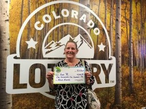 Anna R. holding an oversized check for $1,500 in front of Colorado Lottery background