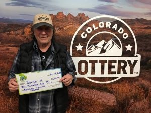 Donald M. sosteniendo el cheque de $1,000 frente al fondo de Colorado Lottery