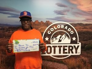 Brian D. holding an oversized check for $5,000 in front of Colorado Lottery background