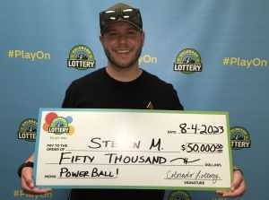 Steven M. de Highlands Ranch sostiene un cheque de gran tamaño por $50,000 frente al fondo de la Lotería de Colorado.