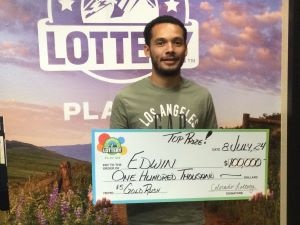 Edwin C. sosteniendo un cheque gigante de $100,000 frente al fondo de la Lotería de Colorado