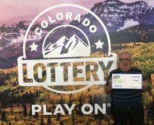John P. sosteniendo el cheque de $1,000 frente al fondo de Colorado Lottery