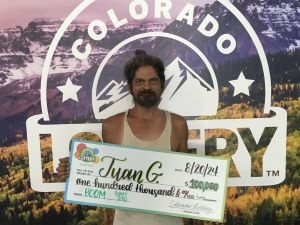 Juan G. sosteniendo un cheque de gran tamaño por $100,000 frente al fondo de la Lotería de Colorado