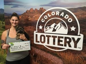 Makayla B. of Englewood holding an oversized check for $10,000 in front of Colorado Lottery background
