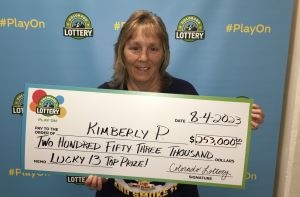 Kimberly P. de Denver sosteniendo un cheque de gran tamaño por $253,000 frente al fondo de la Lotería de Colorado.