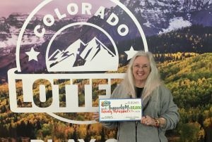 Amanda M. sosteniendo su cheque de gran tamaño por $20,000 frente al fondo de la Lotería de Colorado