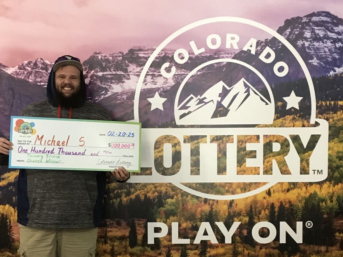 Michael S. sosteniendo un cheque de gran tamaño frente a un fondo de la Lotería de Colorado