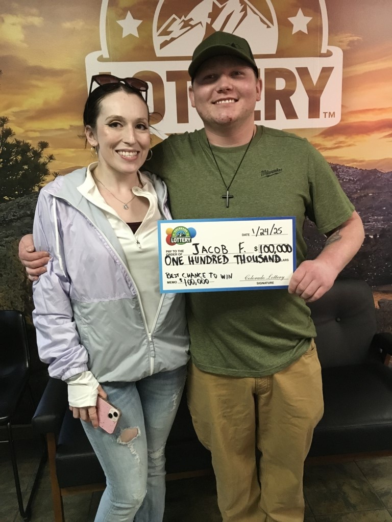Jacob F. sosteniendo un cheque por $100,000 frente al fondo de la Lotería de Colorado.