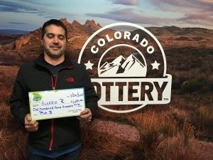 Álvaro R. sosteniendo un cheque de gran tamaño por $1,450 frente al fondo de la Lotería de Colorado