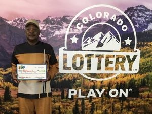 Nathaniel L. sosteniendo el cheque gigante de $10,000 frente al fondo de Colorado Lottery
