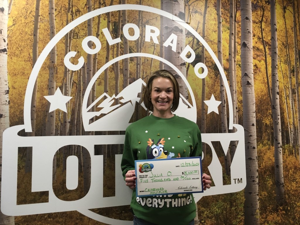Julia O. holding oversized check for $5,000 in front of Colorado Lottery background