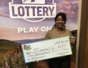Maribel J. de Glenwood Springs sosteniendo un cheque de gran tamaño por $1,000 frente al fondo de la Lotería de Colorado