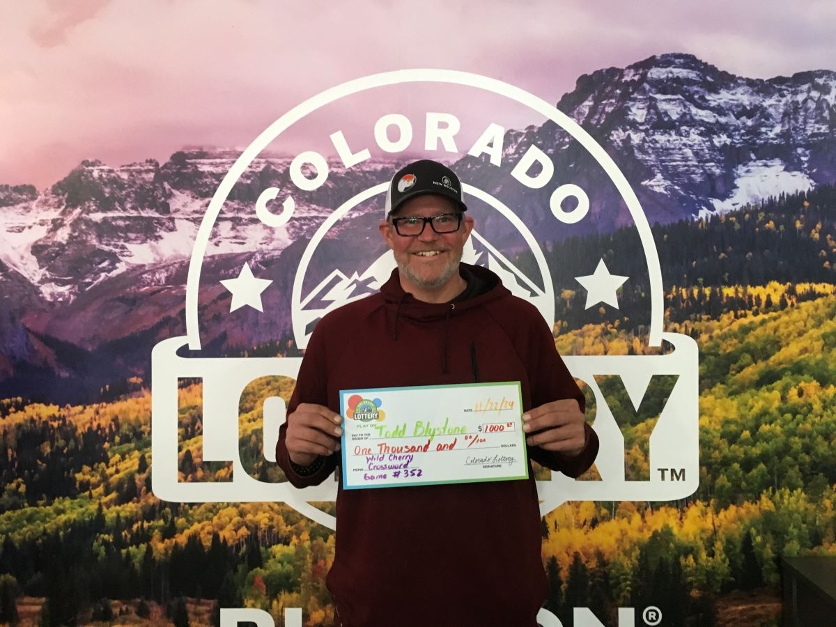 Todd B. holding an oversized check for $1,000 in front of Colorado Lottery background