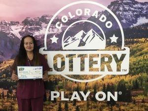 Diana T. sosteniendo un cheque gigante de $2,000 frente al fondo de la Lotería de Colorado.