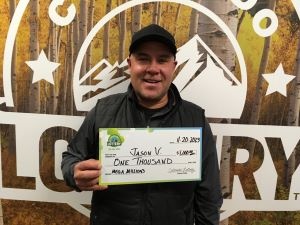 Jason V. sosteniendo el cheque de $1,000 frente al fondo de Colorado Lottery