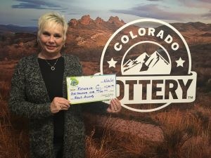 Katherine S. sosteniendo el cheque gigante de $1,000 frente al fondo de Colorado Lottery