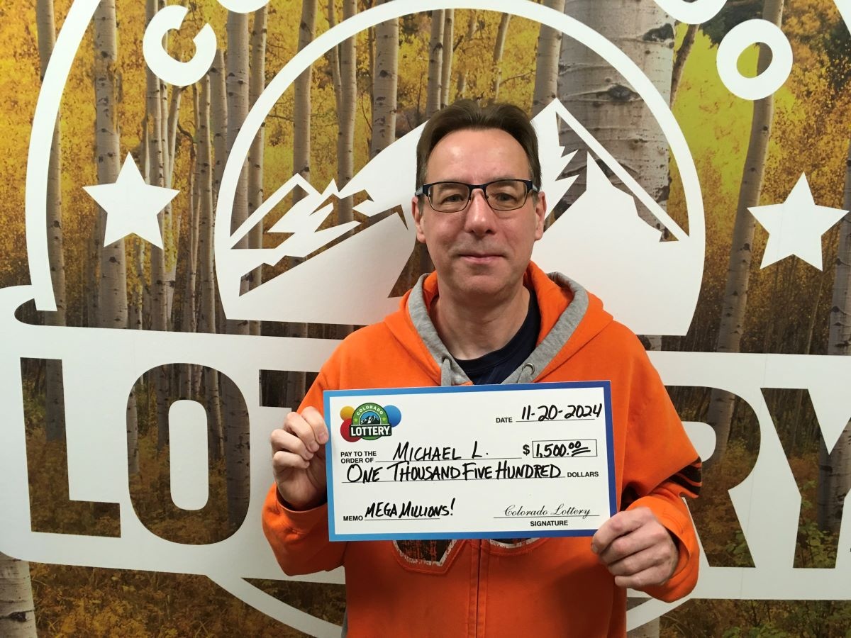Michael L. holding an oversized check for $1,500 in front of Colorado Lottery background