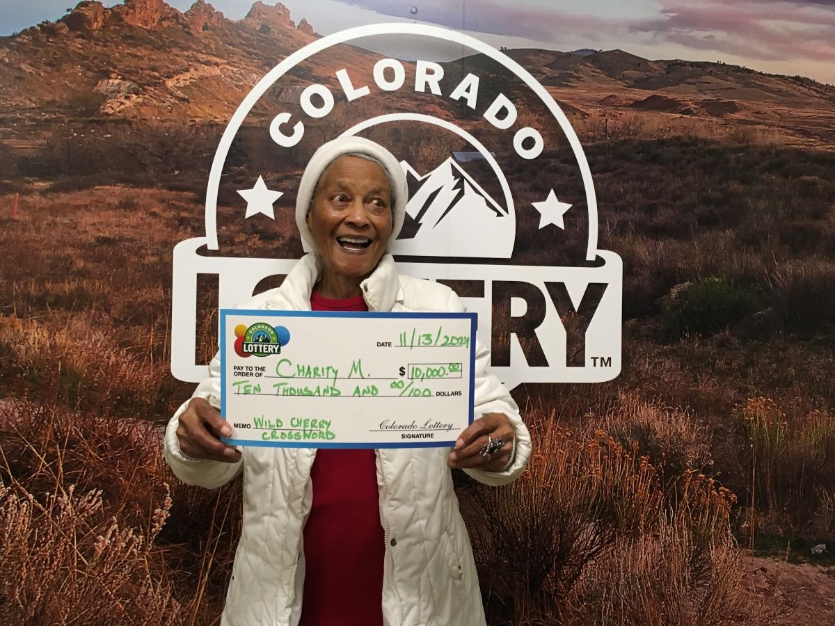 Charity M. holding an oversized check for $10,000 in front of Colorado Lottery background