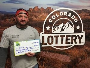 William D. sosteniendo un cheque de gran tamaño por $5,000 frente al fondo de la Lotería de Colorado