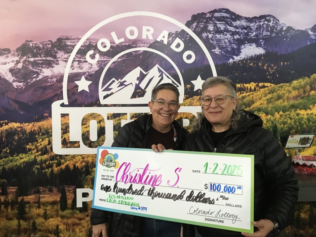 Christine S. sosteniendo un cheque por $100,000 frente a un fondo de la Lotería de Colorado.