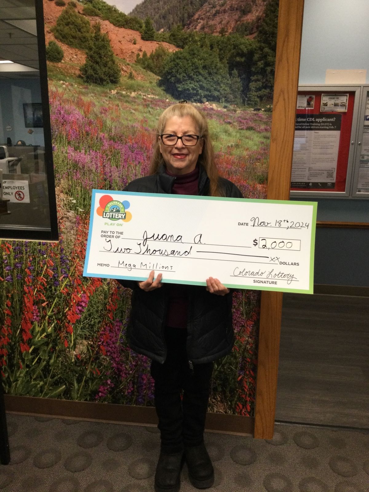 Juana A. sosteniendo el cheque gigante de $2,000 frente al fondo de Colorado Lottery