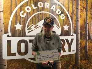 Dennis W. sosteniendo el cheque gigante de $20,000 frente al fondo de Colorado Lottery