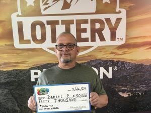 Darryl E. sosteniendo el cheque gigante de $50,000 frente al fondo de Colorado Lottery