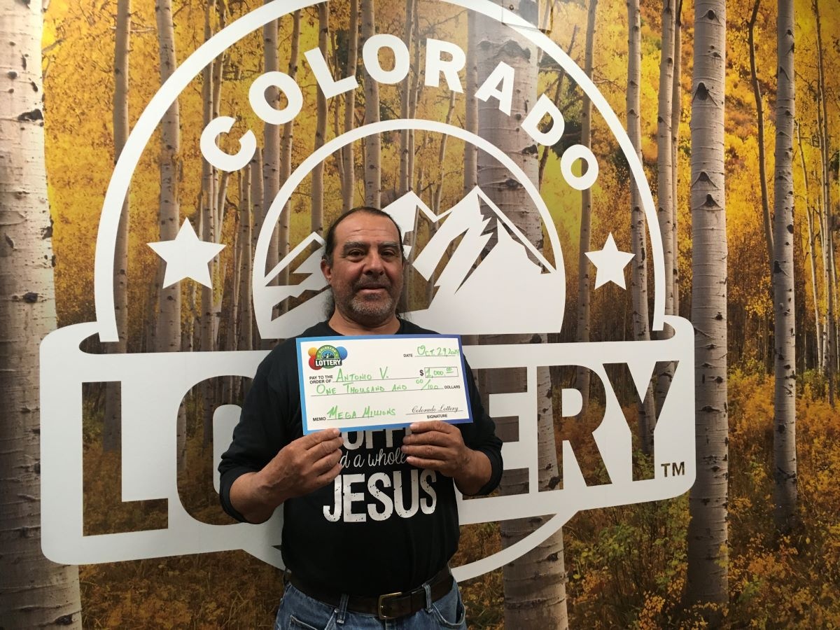 Antonio V. sosteniendo el cheque gigante de $1,000 frente al fondo de Colorado Lottery